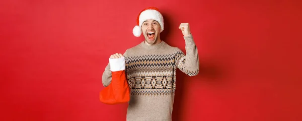 Conceito de férias de inverno, ano novo e celebração. Homem surpreso e feliz gritando de alegria, presente encontrado dentro de Natal meia e torcida, levantando a mão para cima e sorrindo — Fotografia de Stock