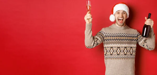 겨울 휴가, 크리스마스, 그리고 축하 행사의 개념. 스웨터와 산타 모자를 입고 멋진 남자, 새해 파티를 즐기고 유리와 샴페인 병을 들고 즐기는 — 스톡 사진