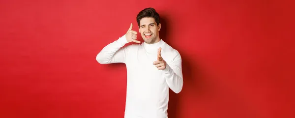 Portrait of sassy and confident handsome man, flirting with you, asking to call him, showing phone sign and pointing at camera, standing over red background — Stock Photo, Image