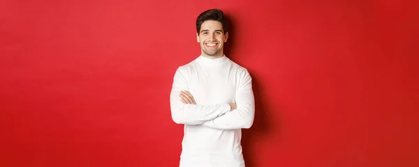 Concept of winter holidays, christmas and lifestyle. Portrait of confident good-looking man with bristle, wearing white sweater, cross arms on chest and smiling satisfied — Stock Photo, Image