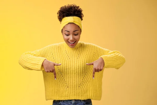 Impresionante entusiasta sonriente fascida afroamericana mujer en jersey diadema mirada apuntando hacia abajo dedos índice jadeando asombrado fascinado fresco emocionante promo, de pie fondo amarillo — Foto de Stock