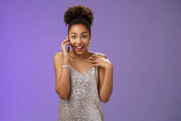 Impressed talkative charming african-american woman in shiny silver evening dress pointing herself amused surprised smiling talking smartphone widen eyes astonished, standing blue background