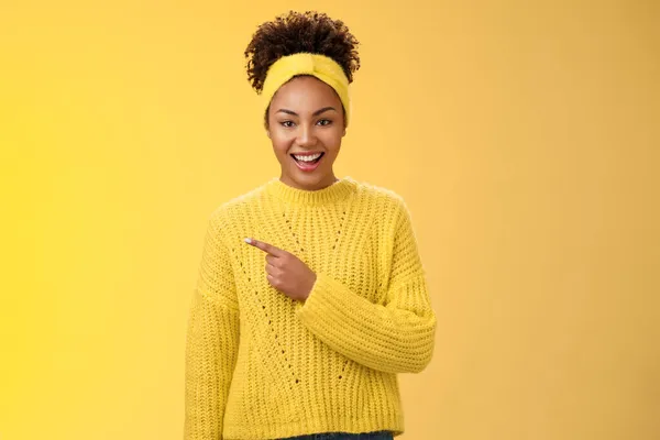 Amistosa chica encantadora entusiasta de buen aspecto negro en suéter de diadema sonriendo ampliamente divertido apuntando a la izquierda impresionante lugar que le muestra el espacio en blanco perfecto anuncio, posando fondo amarillo — Foto de Stock