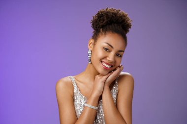 Tender elegant wealthy young african american rich woman in brilliants silver stylish shiny dress lean head shoulder smiling flirty romantic gaze camera standing amused blue background clipart