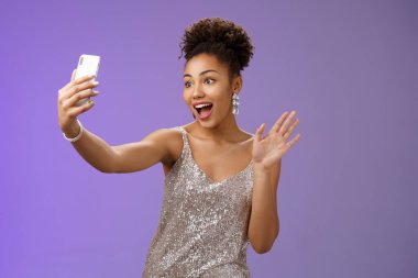 Dost canlısı, kendine güvenen, gümüşten parıltılı elbisesi olan Afro-Amerikan kadın. Palmiye sallıyor. Merhaba.