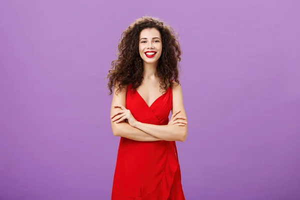 Χαριτωμένη φιλόδοξη και ευτυχισμένη όμορφη γυναίκα της Ευρώπης σε πολυτελές κόκκινο φόρεμα κρατώντας τα χέρια σταυρωμένα σε αυτοπεποίθηση χειρονομία χαμογελώντας ευρέως έχοντας κόμμα γιορτάζει αποφοίτηση πάνω από μωβ φόντο — Φωτογραφία Αρχείου