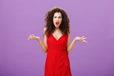 Woman being shocked guy breaking up with her during party. Concerned pissed and outraged good-looking lady in red dress with evening makeup shrugging with spread palms in clueless and questioned pose