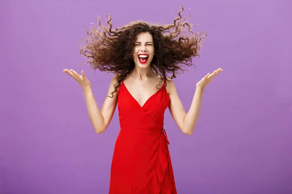 Εκφράζοντας την εσωτερική αγριότητα. Πορτρέτο της άγριας και ξέγνοιαστες γοητευτικό ευρωπαϊκό θηλυκό σε κομψό βράδυ κόκκινο φόρεμα flicking σγουρά μαλλιά με υψωμένα χέρια γελώντας δυνατά απολαμβάνοντας τον εαυτό της κατά τη διάρκεια του κόμματος — Φωτογραφία Αρχείου