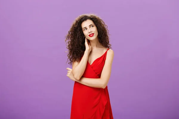 魅力的で優しいですエレガントな女性で巻き毛でスタイリッシュな夜の赤いドレス傾斜頭を触れ首と右上隅の入札を見て、白昼夢上の紫色の背景 — ストック写真