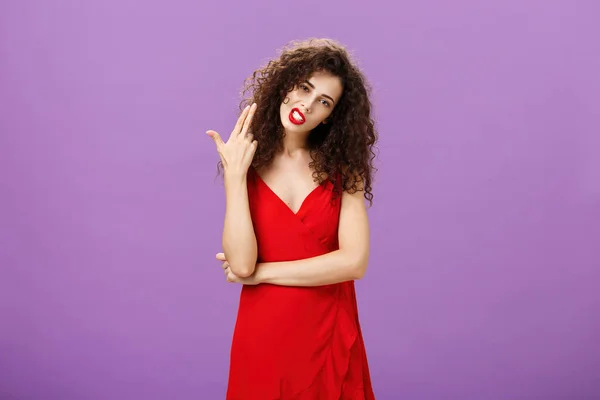 Κανόνες που με σκοτώνουν. Επαναστατική ζεστό και κομψό ευρωπαϊκή γυναίκα σε κομψό κόκκινο φόρεμα με σγουρά μαλλιά κλίση κεφάλι δείχνει χειρονομία όπλο δάχτυλο σαν να φυσάει μυαλά από πλήξη πάνω από μωβ φόντο — Φωτογραφία Αρχείου