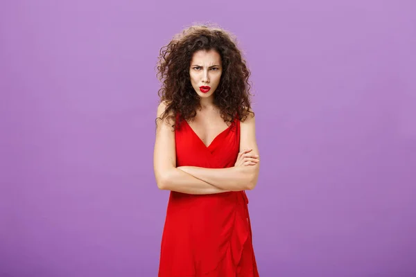 Estudio de disparo de mujer indignada disgustada y ofendida en elegante vestido de noche rojo cruzando brazos contra el pecho frunciendo el ceño mirando desde debajo de la frente con ira, mostrando defensividad siendo criticado — Foto de Stock