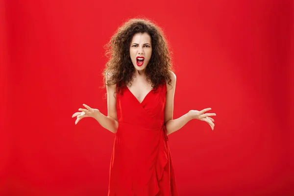 Dissatisfied angry and pissed attractive curly-haired female in stylish red dress arguing and frowning being bothered and in fury while fighting with boyfriend being shocked dinner ruined — ストック写真