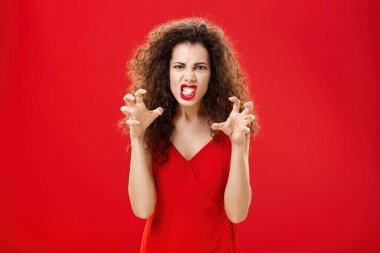 Woman like panter wanting scratch eyes of enemy. Portrait of pissed angry and pressured fed up woman clenching teeth and hands as if choking enemy with hate and anger in eyes being scary over red wall