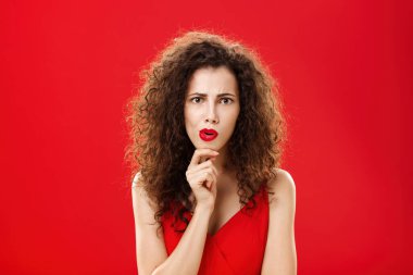 Odaklanmış ve endişeli, kıvırcık saçlı, kıvırcık saçlı, kıvırcık dudaklı, çenesini ovuşturan, kameraya kararlı bakışlı, düşünceli ve endişeli bir dedikoducu kız. Şok edici konuşmaları dikkatlice dinliyor ya da dinliyor.