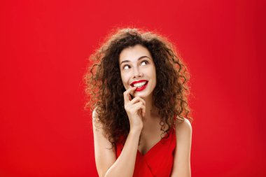 Sevimli, karizmatik ve narin, kıvırcık saçlı, kırmızı elbiseli, parmaklarını ısıran, gözlerinde arzuyla gülümseyen, sağ üst köşedeki hayalperest kadın.