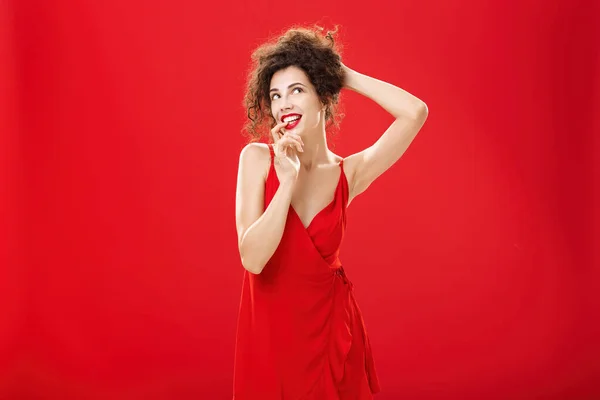 Mulher caucasiana sonhadora e elegante em vestido de festa elegante pentear o cabelo segurando fios encaracolados com mão mordendo o dedo flertando olhando no canto superior direito nostálgico, sonhando acordado — Fotografia de Stock