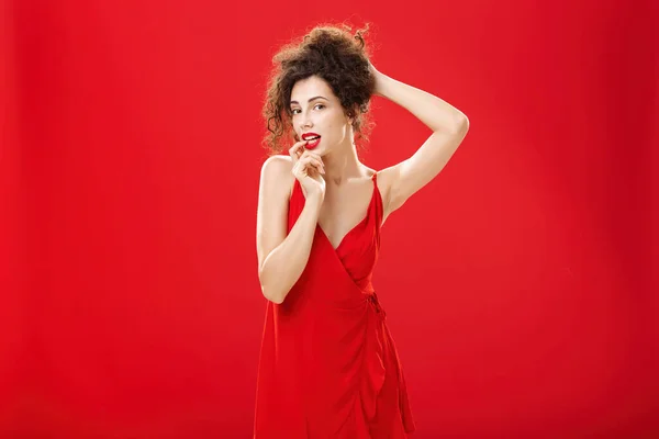 Γοητευτικό και αισθησιακό κομψό πλούσια κυρία σε κόκκινο φόρεμα βράδυ χτένισμα των μαλλιών σε πολυτελές χτένισμα των μαλλιών αγγίζοντας lip flirty στέκεται πάνω από στούντιο φόντο forplaying με το σύζυγο μετά από ρομαντικό δείπνο — Φωτογραφία Αρχείου