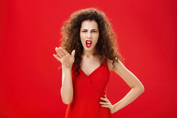 Girl chowing her temper to employees being fed up with unappropriate behaviour complaining standing pissed and dissatisfied gesturing with palm and holding hand on hip over red background — стоковое фото