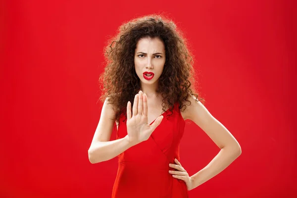Počkej, počkej. Intenzivní vážně vypadající nespokojená dospělá žena s kudrnatými vlasy ve stylových červených šatech mračící se zvedající dlaň v žádném gestu odmítající dát negativní odpověď, zakazující přijít blíž — Stock fotografie