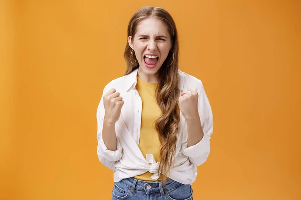 Chica sensación de poder superar cualquier problema gritando para animar y aumentar la confianza apretando los puños levantados en alegre y gesto de victoria gritando en voz alta, liberando el estrés contra el fondo naranja —  Fotos de Stock