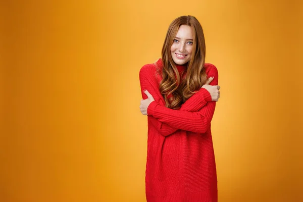 Mujer pelirroja romántica suave y tierna en suéter de punto rojo sintiéndose acogedora y cálida abrazándose y sonriendo linda, sensual a la cámara mirando encantada sobre fondo naranja — Foto de Stock