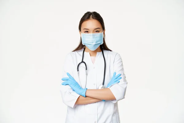Kép a hivatásos orvos, ázsiai nő orvos arc orvosi maszk, gumikesztyű, álló karok keresztbe, fehér háttér — Stock Fotó