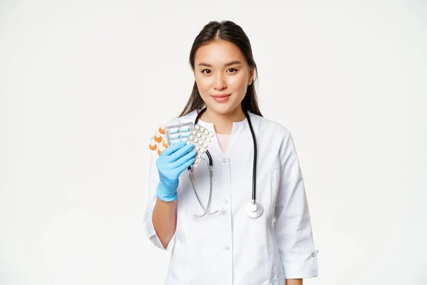 Zdravotní a lékařská koncepce. Asijský lékař ukazuje pilulky, vitamíny v gumové sterilní rukavice, stojící v uniformě přes bílé pozadí — Stock fotografie