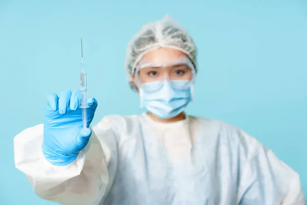 Vaccination and covid-19 컨셉트. 의료 종사자, 이시아인 의사, 코로나 바이러스 백신을 주사기로 보여 주는 모습, 개인 보호 장비를 착용하고 얼굴에 마스크를 착용하고 푸른 배경을 가진 모습 — 스톡 사진