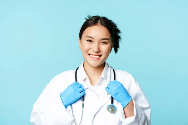 Asijky žena lékař, zdravotní sestra s úsměvem sebevědomý, nastavení stetoskop na krku, stojící v lékařské uniformě přes modré pozadí — Stock fotografie