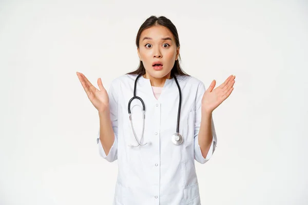 Şaşırmış doktor görüntüsü, el kaldırıyor ve şok olmuş görünüyor, hastane üniforması içinde duruyor, beyaz arka plan. — Stok fotoğraf