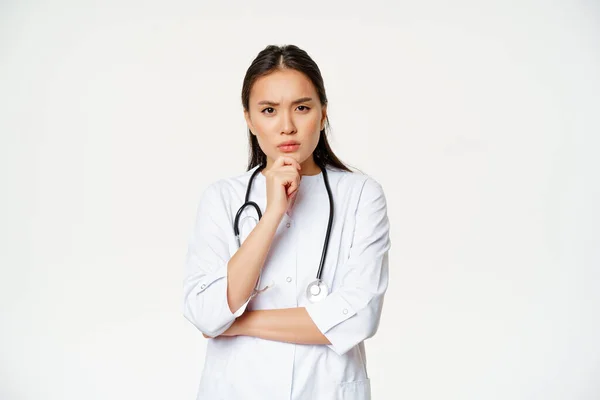 Asijské ženy lékař v uniformě myšlení, vypadající vážné a znepokojené, dotýkat bradu při přemýšlení, naslouchat pacient v nemocnici, bílé pozadí — Stock fotografie