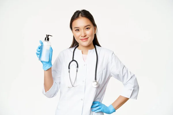 Portrét asijské ženy lékař, lékař doporučující ruční dezinfekci pro prevenci covid-19, drží láhev s gumovými rukavicemi, bílé pozadí — Stock fotografie