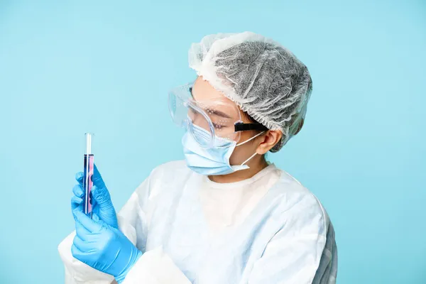 시험관에서 화학 물질을 혼합하는 실험실 근로자, 개인 보호 장비와 안전망을 착용하고 있는 모습, 푸른 배경 — 스톡 사진