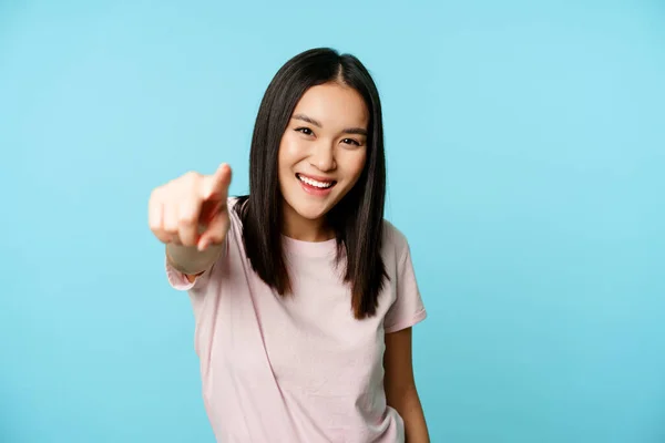 És tu. Sorrindo feliz asiático mulher apontando dedo para a câmera, parabenizando, convidando as pessoas, de pé em t-shirt sobre fundo azul — Fotografia de Stock