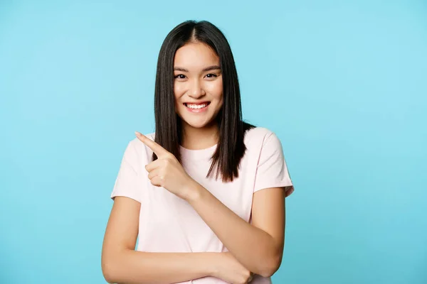 Retrato de modelo femenino asiático sonriente feliz, apuntando a la esquina superior izquierda, mostrando banner de venta, anuncio de tienda, fondo azul — Foto de Stock