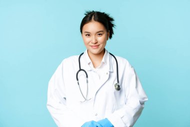 Sağlık ve tıbbi konsept. Hastane üniformalı ve steteskoplu gülümseyen Asyalı kadın doktor, hastaya hoş görünüyor, mavi arka plan.