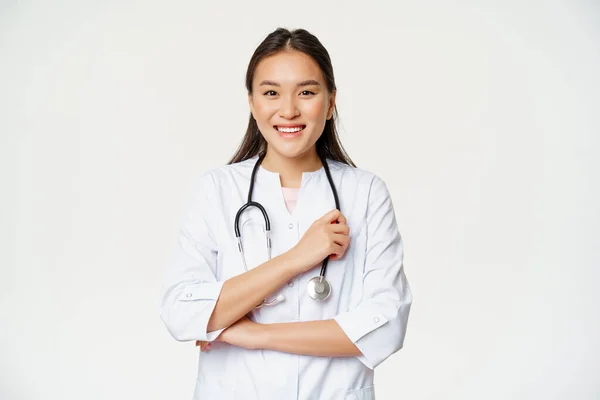 Zdravotní a nemocniční koncept. Usmívající se asijský lékař, žena zdravotní sestra v uniformě, šťastný pohled na kameru, stojící nad bílým pozadím — Stock fotografie