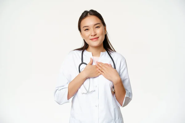 Obrázek ženského lékaře pečujícího o pacienty, držícího se za ruce na srdci, příjemně se usmívajícího, stojícího v lékařské uniformě na bílém pozadí — Stock fotografie