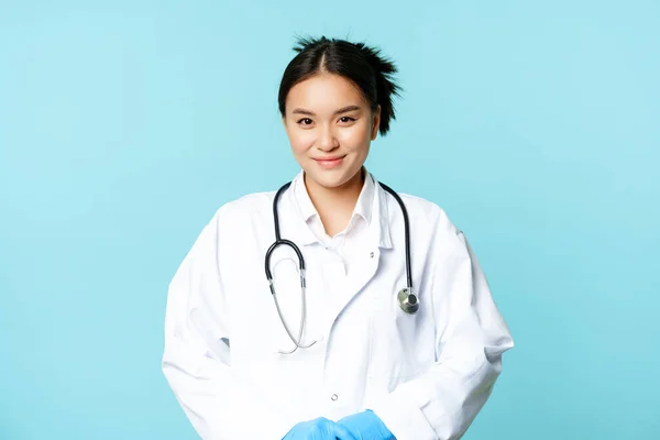 Cuidados de saúde e conceito médico. Sorrindo asiático médico feminino no hospital uniforme e estetoscópio, olhando agradável para paciente, fundo azul — Fotografia de Stock