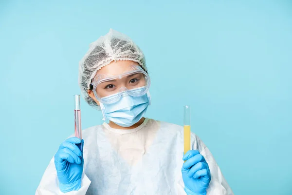 실험 과 의학 실험의 개념이다. 미소짓는 이시아 여성 의사, 임상 실험 제품 이 있는 튜브를 보여 주는 실험실 직원, 푸른 배경 — 스톡 사진