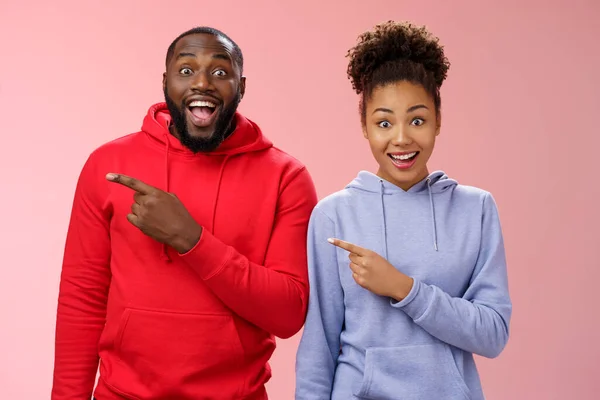 Impressed two best friends african american man woman 25s drop jaw amused visit awesome interesting park pointing left index fingers widen eyes thrilled having fun together, standing pink background — Stock Photo, Image