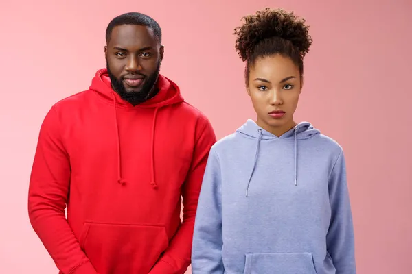Two cute african american siblings standing together pink background invited family dinner greet new mom boyfriend, sister look displeased serious brother smug have idea prank stepdad
