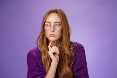 Dedektif gibi kız arkadaş bulmacayı çözüyor, varsayımlar yapıyor, gözlerini kısıyor, sola bakıyor, azimli ve düşünceli gözlükler takıyor, mor arka plan üzerinde düşünürken çeneye dokunuyor.