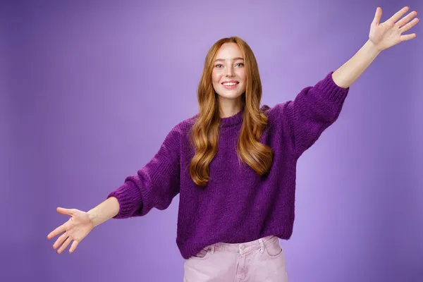 Chica extendió las manos hacia los lados para dar la bienvenida y saludar a un amigo dando un cálido abrazo sonriendo ampliamente a la cámara de pie alegre con ganas de abrazo sobre el fondo púrpura, usando suéter violeta y pantalones —  Fotos de Stock