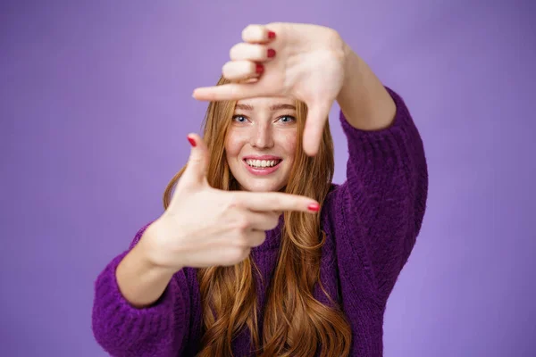 Immagina se. Ritratto di speranzoso e spensierato creativo affascinante rossa 20 donna mostrando cornice con le mani tirate e sorridendo attraverso di essa come immaginando futuro luminoso e felice su sfondo viola — Foto Stock