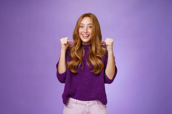 Sim, conseguimos. Jovem feliz e alegre bonita ruiva 20s menina em camisola roxa sobre fundo violeta levantando punhos cerrados em alegria e triunfo, celebrando o sucesso e ganhar, torcendo — Fotografia de Stock