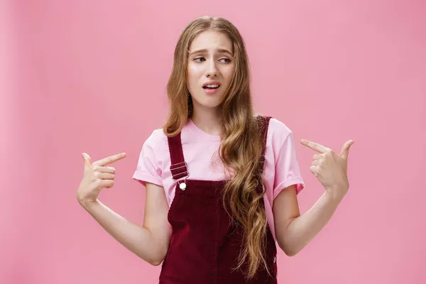 Self-assured arrogant young female student with high ego standing cocky and brag about herself pointing at her with cool snobbish look looking away to right with contempt posing over pink wall — Stock Photo, Image