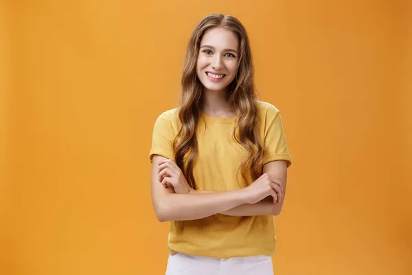 Nazik ve cana yakın genç bayan öğrenci portresi. Dalgalı doğal uzun saçlarıyla el ele tutuşmuş portakal rengi arka planda geniş ve tasasız bir şekilde gülümsüyor. — Stok fotoğraf
