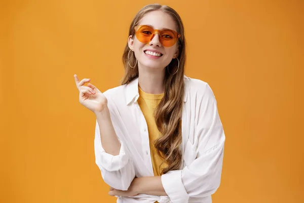 Γυαλιά ηλίου ταιριάζουν στυλ. Πορτρέτο της αυτοπεποίθηση και ανέμελη όμορφη γυναίκα blogger μόδας σε γυαλιά και λευκό t-shirt gesturing με σηκωμένο χέρι και χαμογελώντας χαρούμενα στην κάμερα — Φωτογραφία Αρχείου