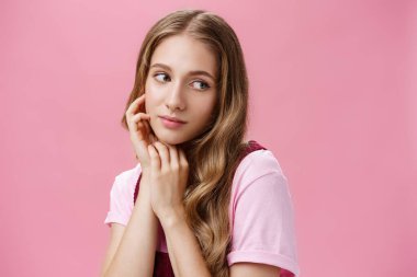 Rüya gibi şehvetli ve kadınsı, doğal saçları dalgalı ve hassas görünüşlü genç bir kadın cilt bakımı ve kozmetik tedavisinden sonra kendini güzel ve narin hisseder ve nazikçe yanağa bakar.